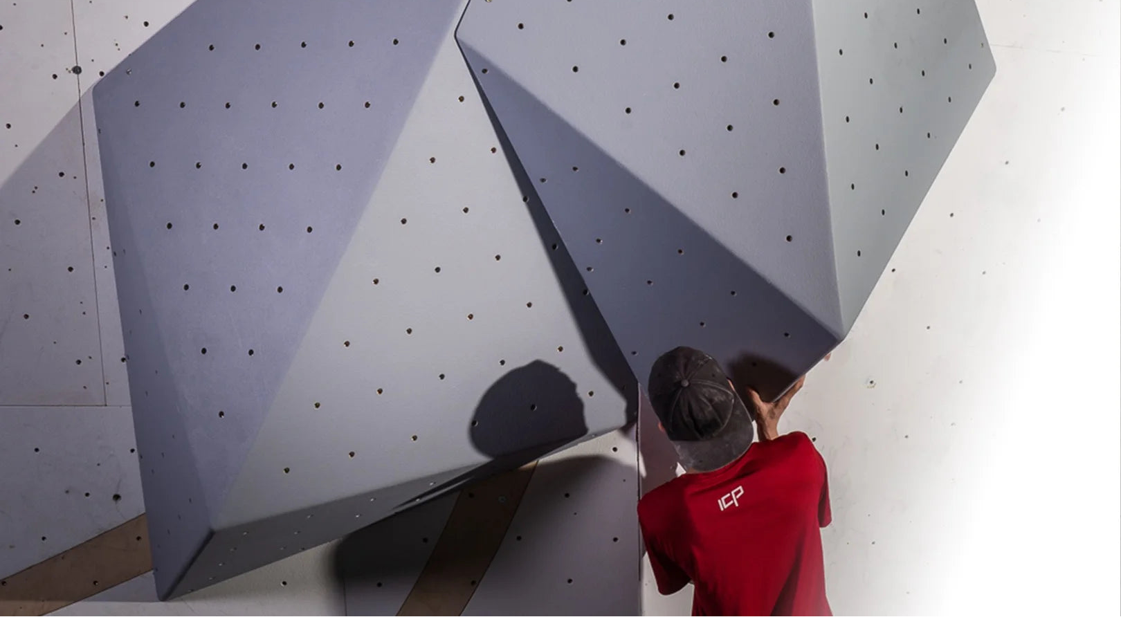 Person setting on geometric rock wall indoors with wooden volumes